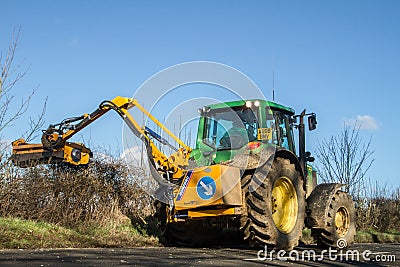 Modern green tractor hedge cutting on road Editorial Stock Photo