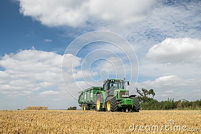 Modern green tractor pulling a trailer in harvest field Editorial Stock Photo