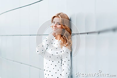 Modern happy positive young woman with beautiful smile in stylish white sweater in the city near bright modern wall. Stock Photo