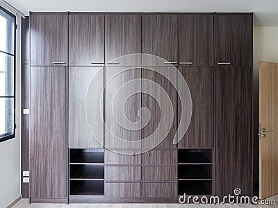 Modern huge brown wooden wardrobe in the white room, closed, front view. Stock Photo