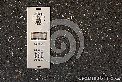 Modern intercom system with numeric keypad, speaker, and camera installed on dark textured stone wall Stock Photo