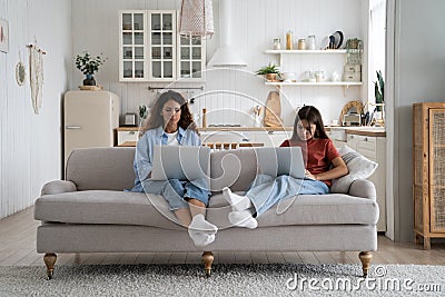 Unsociable introverted woman and teenage girl in casual clothes sits on sofa with laptops on laps Stock Photo