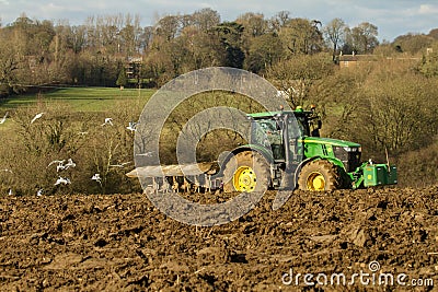 Modern John Deere tractor pulling a plough followed by gulls Editorial Stock Photo