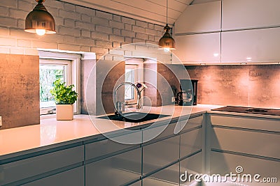 Modern kitchenette with white worktop, black sink and coppery metal lamps Stock Photo