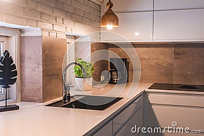 Modern kitchenette with white worktop, black sink and metal lamps Stock Photo