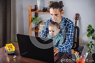 Modern man is working on a laptop, and his little son is sitting on his lap. Concept of family and remote work from home Stock Photo