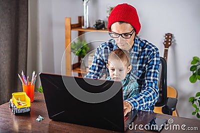 Modern man is working on a laptop, and his little son is sitting on his lap. Concept of family and remote work from home Stock Photo