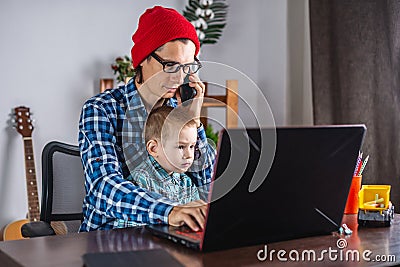 Modern man is working on a laptop, and his little son is sitting on his lap. Concept of family and remote work from home Stock Photo