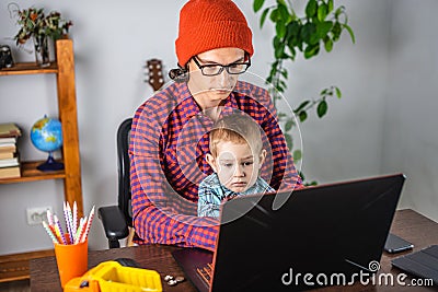 Modern man is working on a laptop, and his little son is sitting on his lap. Concept of family and remote work from home Stock Photo