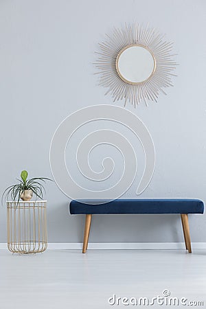 Modern mirror above blue settee and stylish table with plant in golden pot, real photo Stock Photo