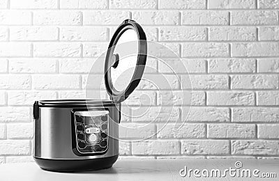 Modern multi cooker on table against brick wall. Stock Photo