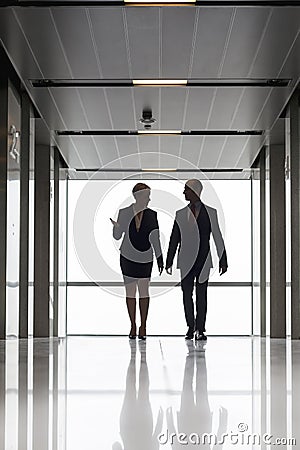 Full length of mature colleagues talking while walking against window in office corridor Stock Photo