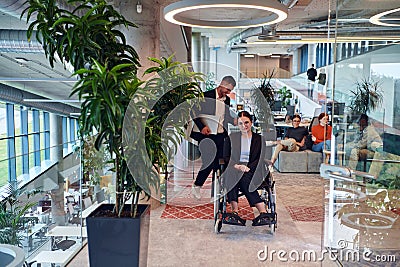 In a modern office, a young businesswoman in a wheelchair is surrounded by her supportive colleagues, embodying the Stock Photo