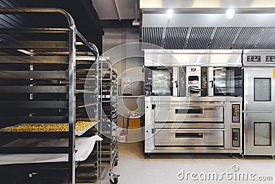Modern pastry kitchen decorated in black, white and steel with baking machine, oven, conveyor, production line, mixer. Stock Photo