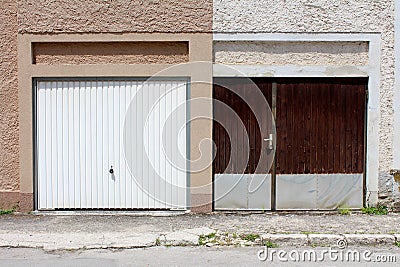 Modern plastic white garage doors on renovated attached family house next to old dilapidated wooden garage doors with metal rain Stock Photo