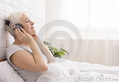 Tranquil senior lady listening to audiobook in bed Stock Photo