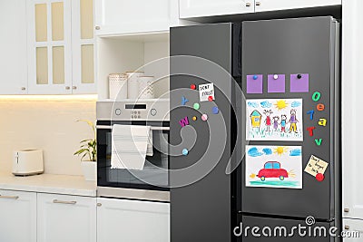 Modern refrigerator with child`s drawings, notes and magnets in kitchen. Space for text Stock Photo