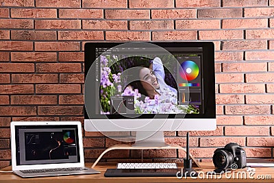 Modern retoucher`s workplace with different digital devices on wooden table near red brick wall Stock Photo