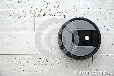 Modern robotic vacuum cleaner removing scattered buckwheat from wooden floor. Space for text Stock Photo