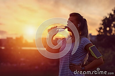 Modern sporty woman drinking water in park at dawn after intense jogging workout Stock Photo