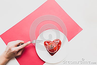 Modern still life scene. Fork in a female hand, tomato in heart shape tomato paste on a white plate. Stock Photo