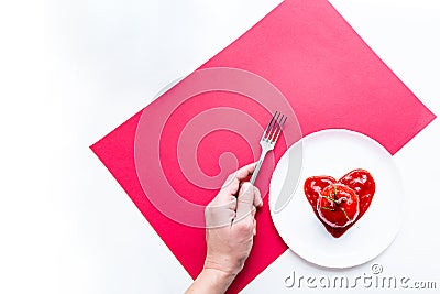 Modern still life scene. Fork in a female hand, tomato in heart shape tomato paste on a white plate. Stock Photo