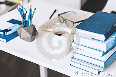 Modern stylish office work place with open book, glasses, office supplies and books, desk work concept in white and blue colors Stock Photo