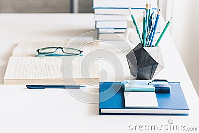 Modern stylish office work place with open book, glasses, office supplies and books, desk work concept in white and blue colors Stock Photo