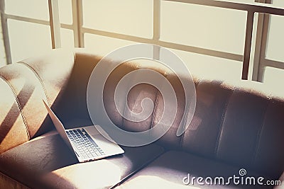Modern sunny coworking loft office, opened laptop computer on a leather sofa, sunlight through a window Stock Photo