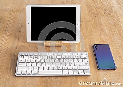 Modern tablet with black screen and white keyboard and design smartphone with triple camera, in a light wood table Editorial Stock Photo