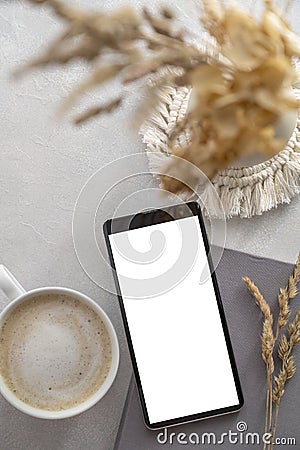 Modern tabletop with with smartphone mockup, cup of coffee, dried plants and notebook on textured white background. Flat lay, Stock Photo