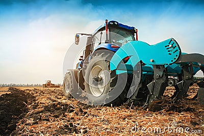 A modern tractor with a trailed plow on the field on a sunny day. Stock Photo