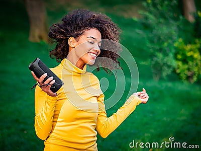 Modern trendy african american girl listening to music by wireless portable speaker.Young beautiful woman enjoying Stock Photo