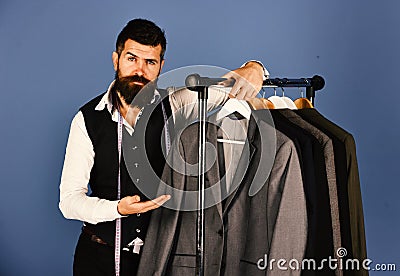 Modern wardrobe choice concept. Designer presents suit near clothes hangers. Man with beard Stock Photo
