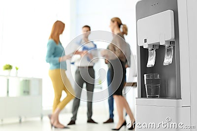 Modern water cooler with glass and blurred office employees on background Stock Photo