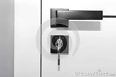 Modern white door with matte black handle and magnetic locks, lock with key inserted. Stock Photo