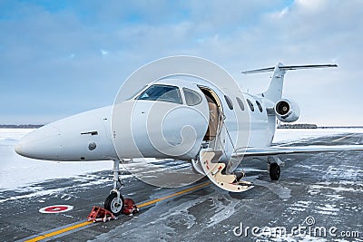 Modern white corporate jet plane with an opened gangway door at the winter airport apron Stock Photo