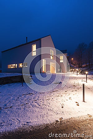 Modern white house with light windows surronded by mountain, snow and trees. Chirstmas mood Stock Photo