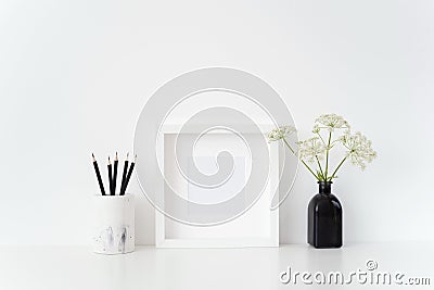 Modern white square frame mockup with a Aegopodium in black vase and black pencils on white background. Stock Photo