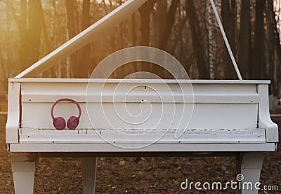 Modern, wireless, pink headphones lie on a white, wooden, old piano, in the evening at sunset in a park. Classic in modern Stock Photo