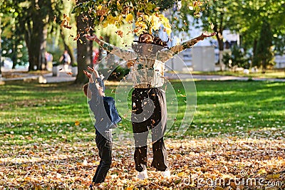 A modern woman joyfully plays with her son in the park, tossing leaves on a beautiful autumn day, capturing the essence Stock Photo