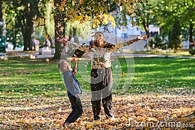 A modern woman joyfully plays with her son in the park, tossing leaves on a beautiful autumn day, capturing the essence Stock Photo