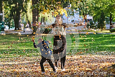 A modern woman joyfully plays with her son in the park, tossing leaves on a beautiful autumn day, capturing the essence Stock Photo