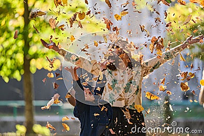 A modern woman joyfully plays with her son in the park, tossing leaves on a beautiful autumn day, capturing the essence Stock Photo