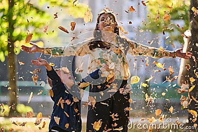 A modern woman joyfully plays with her son in the park, tossing leaves on a beautiful autumn day, capturing the essence Stock Photo