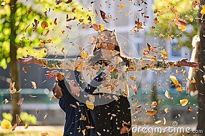 A modern woman joyfully plays with her son in the park, tossing leaves on a beautiful autumn day, capturing the essence Stock Photo