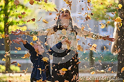 A modern woman joyfully plays with her son in the park, tossing leaves on a beautiful autumn day, capturing the essence Stock Photo