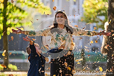 A modern woman joyfully plays with her son in the park, tossing leaves on a beautiful autumn day, capturing the essence Stock Photo