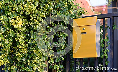 Modern yellow mail box on black fence with beautiful yellows background Stock Photo