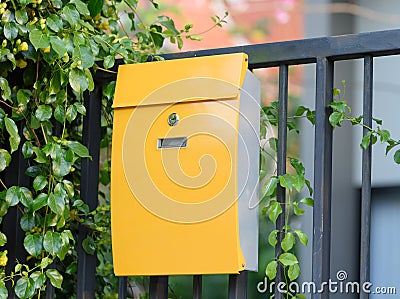 Modern yellow mail box on black fence with beautiful yellows background Stock Photo